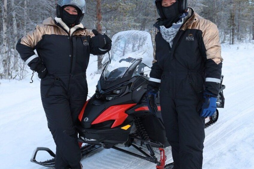 Zwei Personen in Winterkleidung stehen neben einem Schneemobil auf einem verschneiten Weg. 4