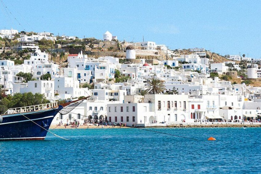 Un pueblo costero con edificios blancos, un bote azul y un mar azul cristalino. 5