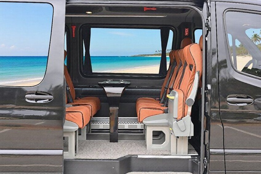 Interior de una camioneta con dos asientos, una mesa central y vista a una playa y al océano. 2