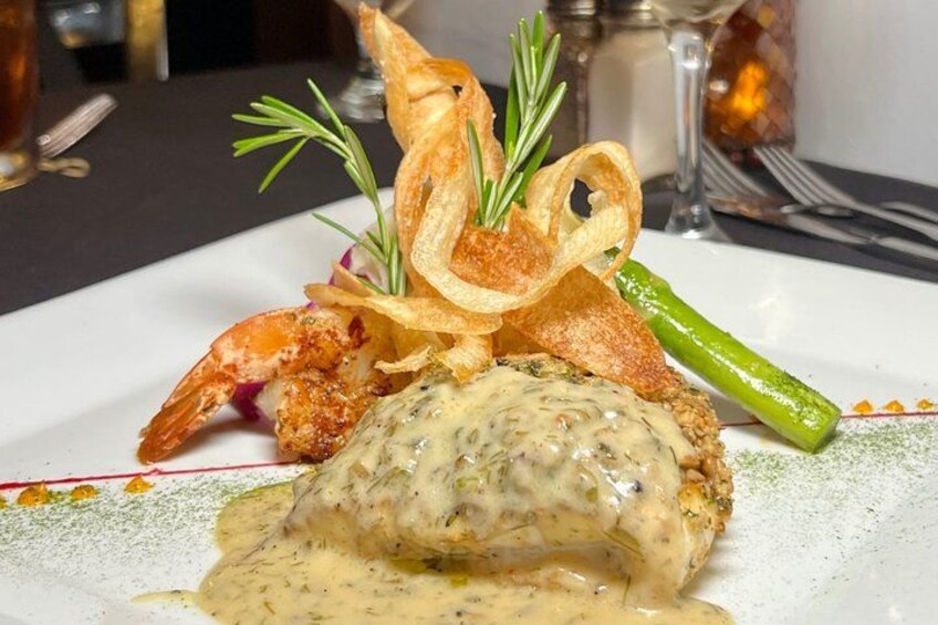 Een bord met een romige saus, garnalen, asperges en een rozemarijn-garnering. 1