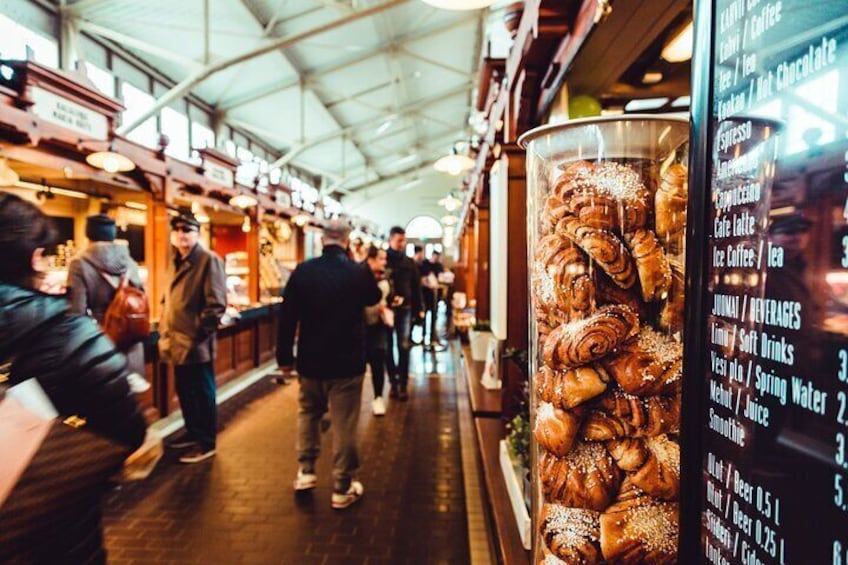A bustling indoor market with people browsing and a menu board displaying food and drink options. 2