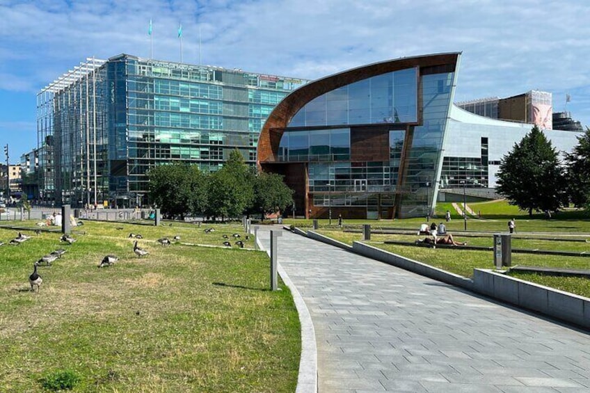 A modern building with a curved glass facade, a paved walkway, and a grassy area with geese. 5