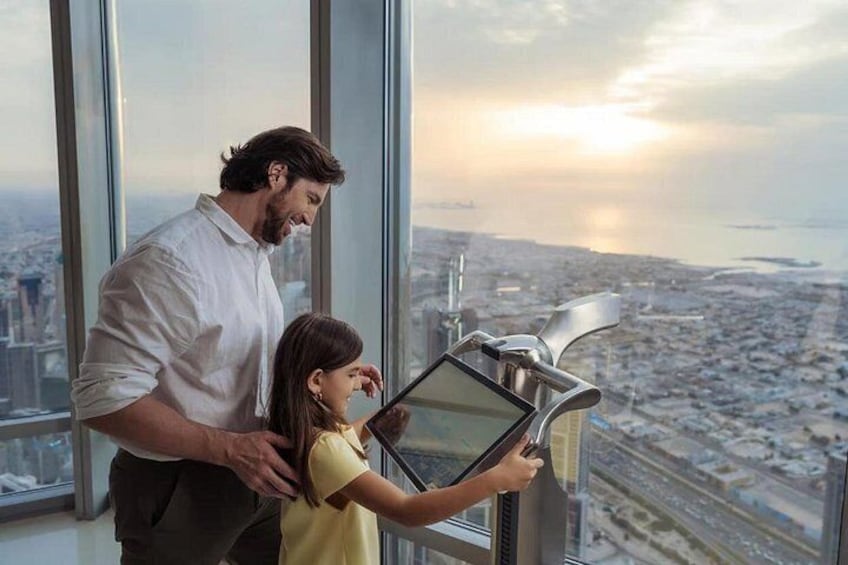 A man and a child looking at a tablet in a high-rise building with a cityscape view. 5