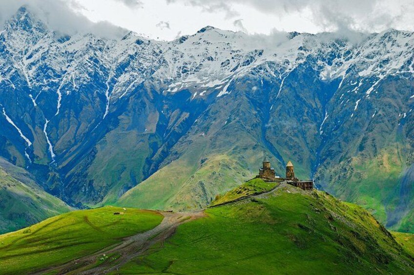 A mountainous landscape with a green valley, a dirt path, and a small stone structure. 3
