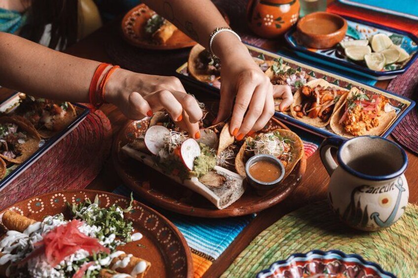 A person preparing tacos with various ingredients and sauces on a colorful table. 2