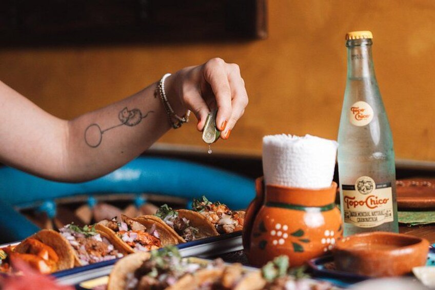 Una persona sirviendo una bebida en un vaso, una botella de Tostito y un plato de tacos. 5