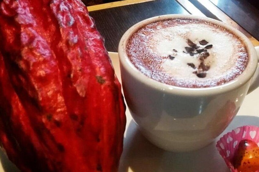 A cup of coffee with a frothy top and chocolate shavings, next to a red chili pepper. 4