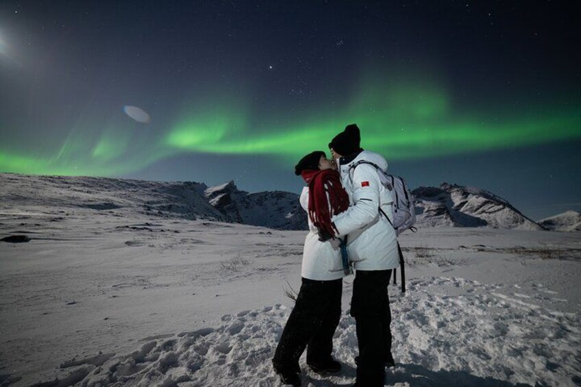 A couple embracing in a snowy landscape with the Northern Lights in the background. 1