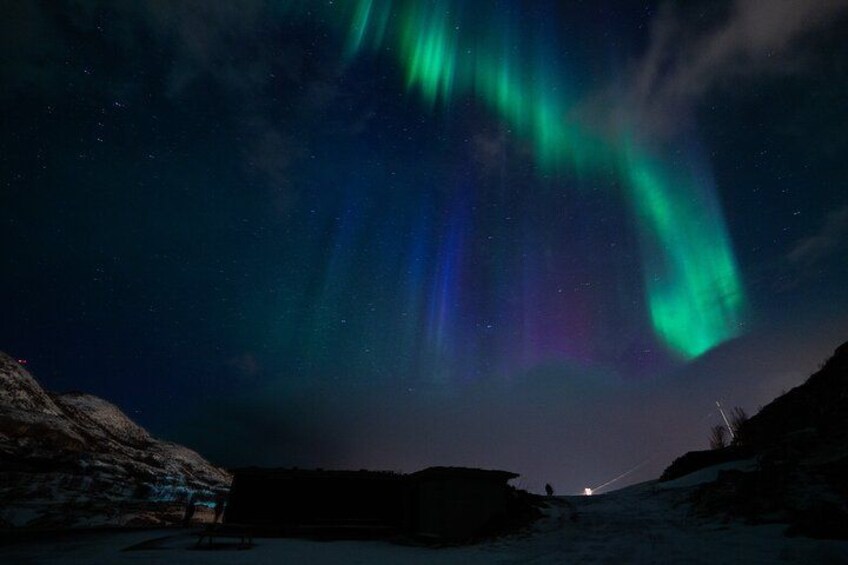 The Northern Lights over a snowy landscape with a distant light source. 5