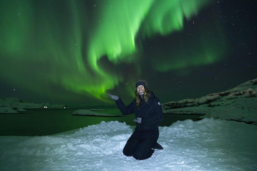 Una persona arrodillada sobre la nieve, con la aurora boreal de fondo. 2