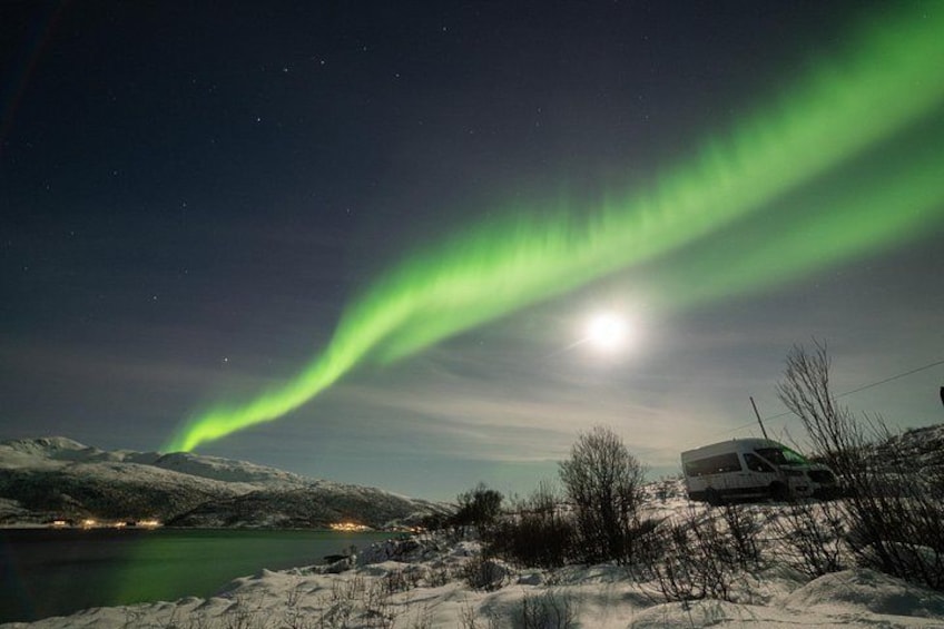 A snowy landscape with a green aurora over a lake and a building in the foreground. 2