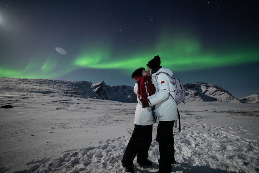 A couple embracing in a snowy landscape with the Northern Lights in the background. 1