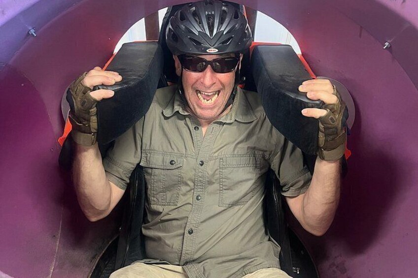A person seated in a roller coaster car, wearing a helmet and gloves. 2