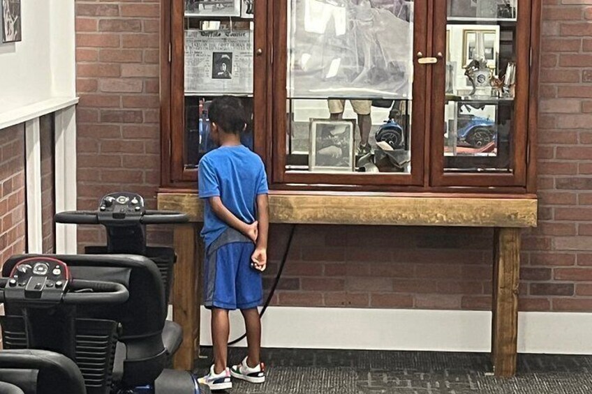 A child standing at a counter in a barber shop with a mirror and various grooming tools visible. 4