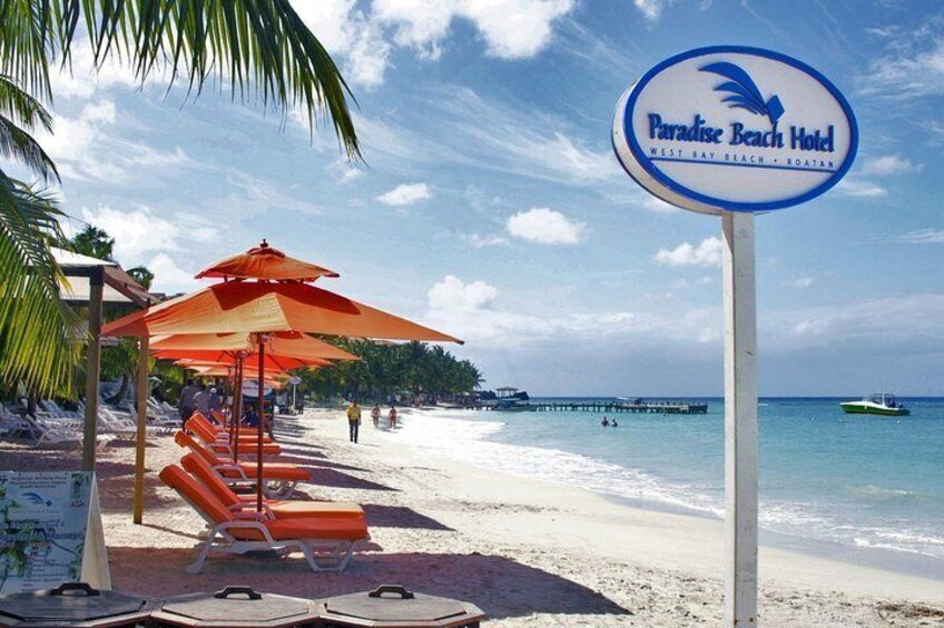 A beach with lounge chairs, a sign for Paradise Beach Hotel, and a pier in the background. 2