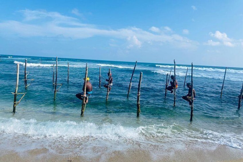 People standing in shallow water with wooden poles, waves crashing onto the shore. 3