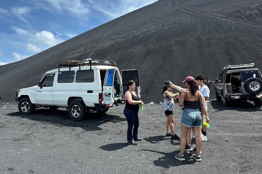 Een groep mensen staat bij een witte auto en een jeep in een vulkaanlandschap. 3