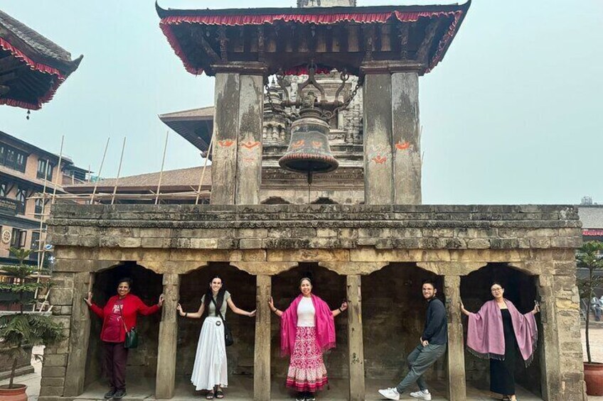 Een groep mensen die poseert voor een traditionele stenen constructie met een klokkentoren. 1