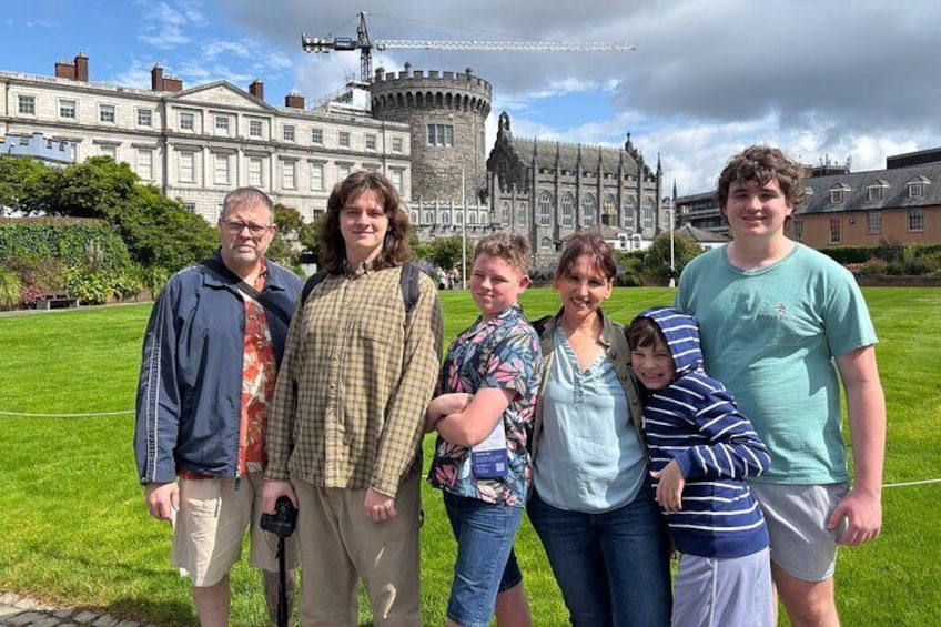 A group of people standing in a grassy area with a historic building in the background. 2