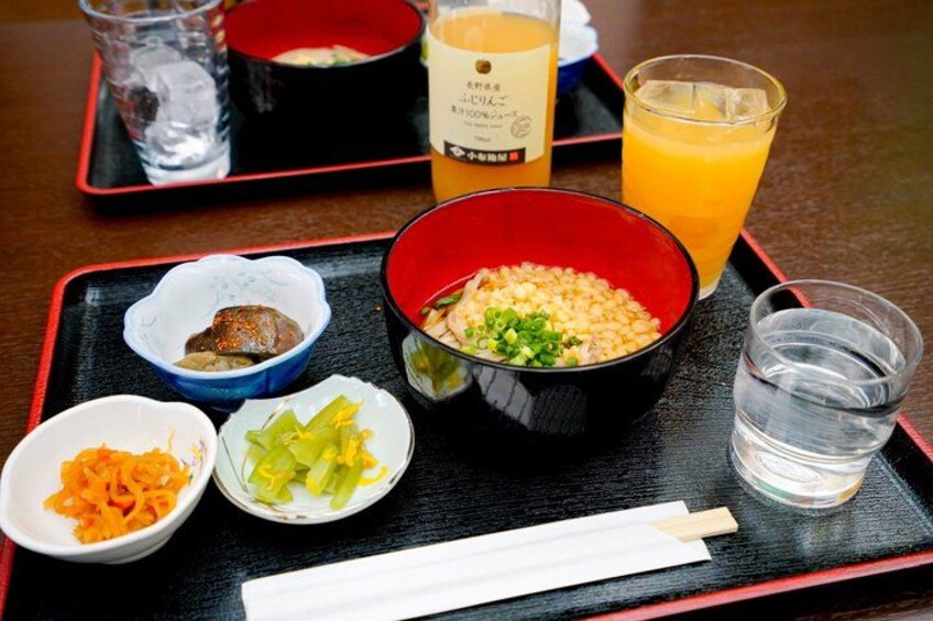 A meal tray with various dishes, including a bowl of rice, a bowl of vegetables, a small dish of pickled vegetables, and a glass of orange juice. 5