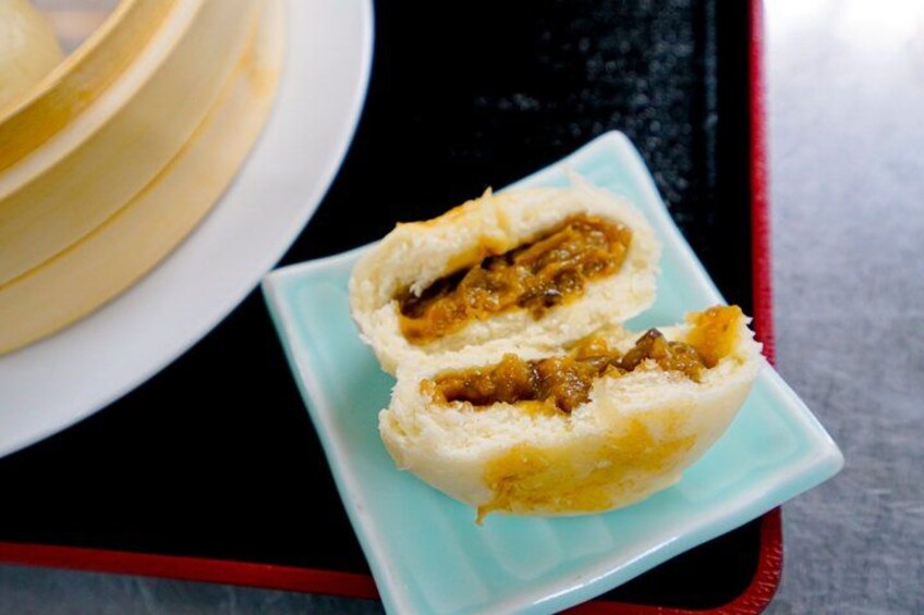 A half-eaten baozi with a savory filling on a light blue plate. 2