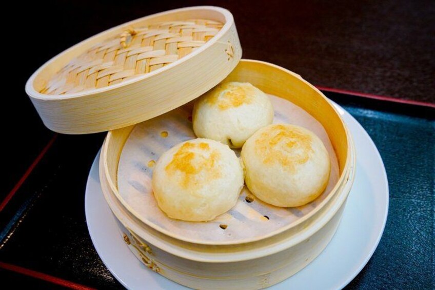 A bamboo steamer with four steamed buns on a white plate. 3