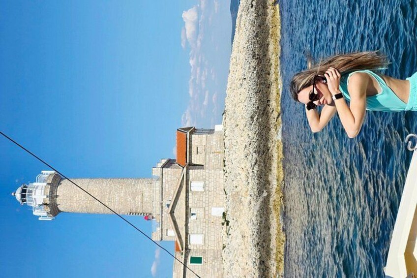 A coastal scene with a lighthouse, a person taking a photo, and a clear blue sky. 2