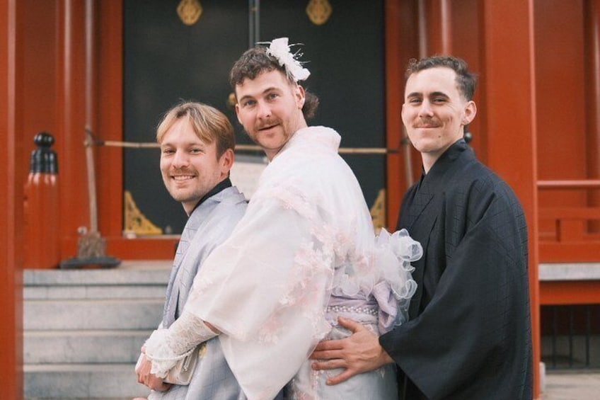A person in a white wedding dress and a person in black attire standing in front of a traditional building with a black door and red walls. 5