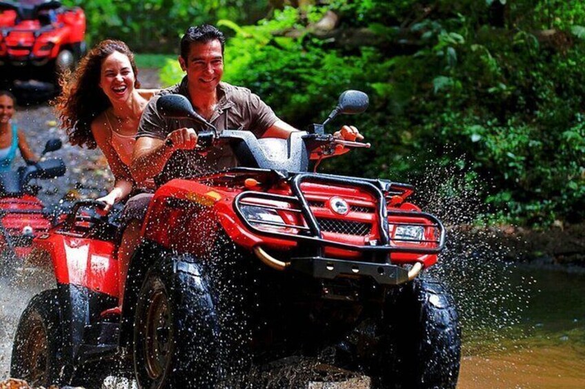 A red ATV with two people riding it, splashing water, surrounded by greenery. 5