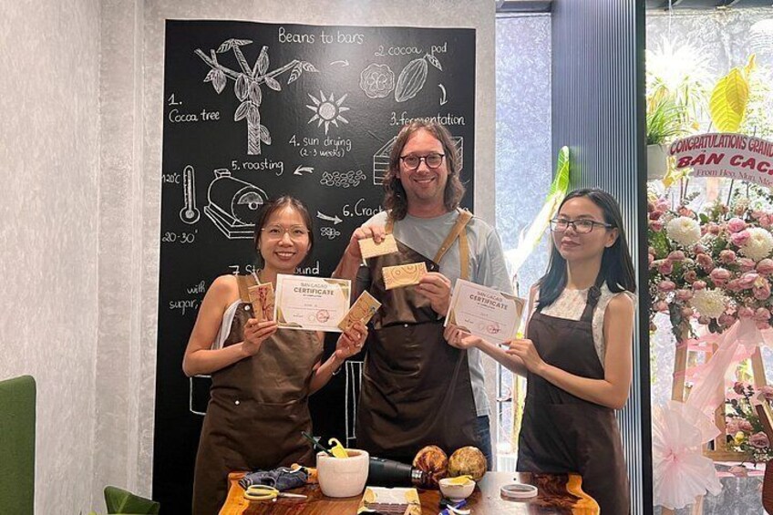 Tres personas sosteniendo certificados frente a una pizarra con ilustraciones sobre café. 3