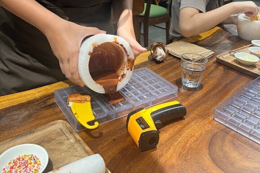 Una persona vertiendo un líquido marrón en un recipiente de plástico transparente sobre una mesa de madera. 5
