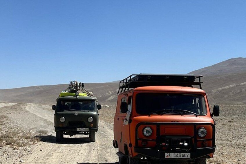 Two off-road vehicles on a dirt road in a barren landscape. 1