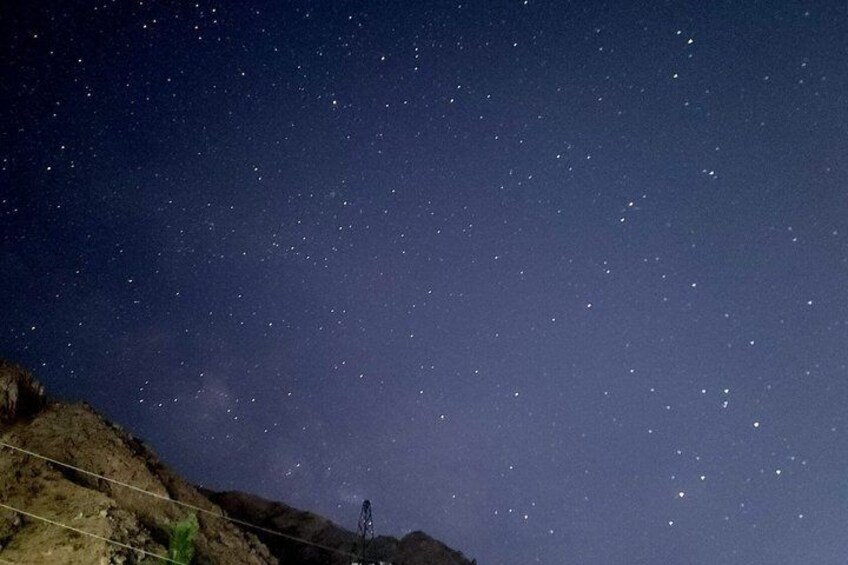 A starry night sky over a rocky landscape with a power line structure. 5