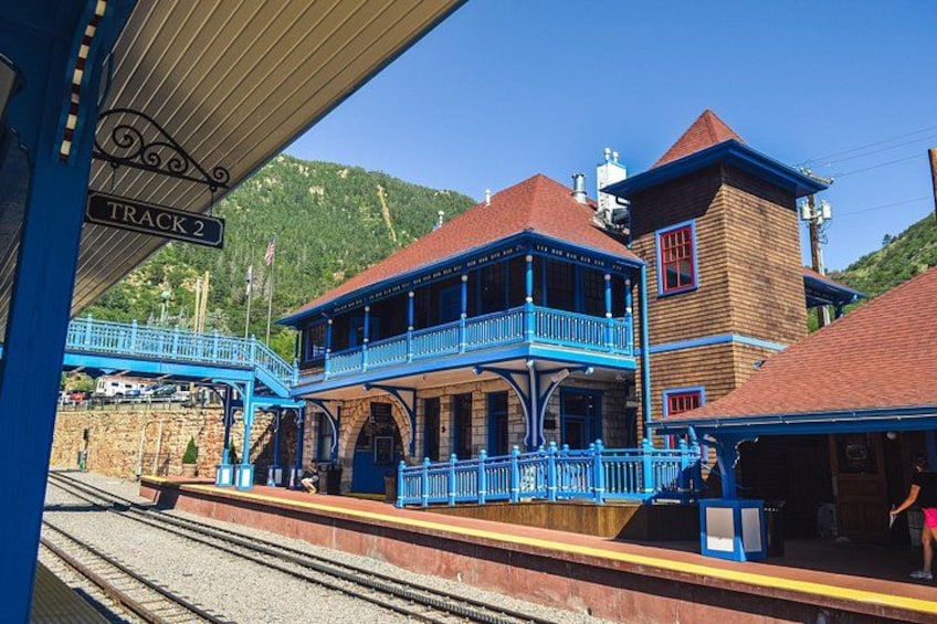 A train station with a wooden building, blue balconies, and a sign reading 'TRACK 2'. 3