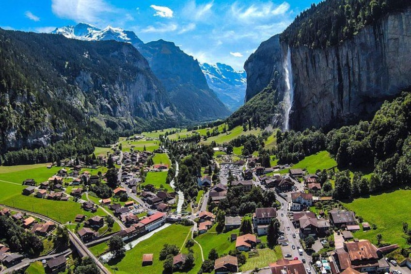 Un pueblo ubicado en un valle con una cascada y montañas al fondo. 2
