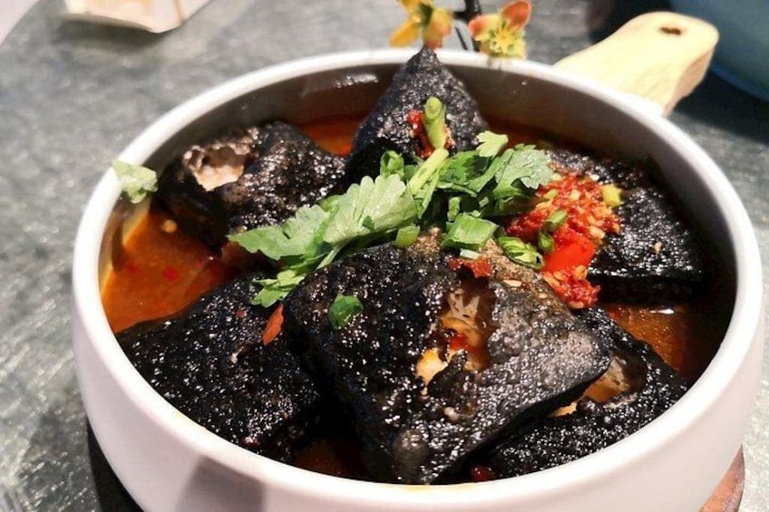 Un tazón de estofado de pescado negro, adornado con hierbas verdes y chiles rojos. 3