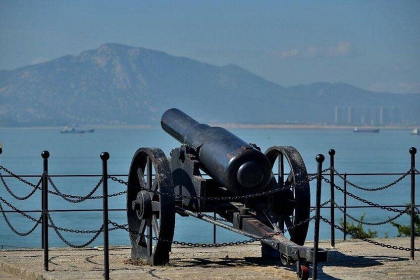 A cannon on display with a chain fence, a body of water, and mountains in the background. 3