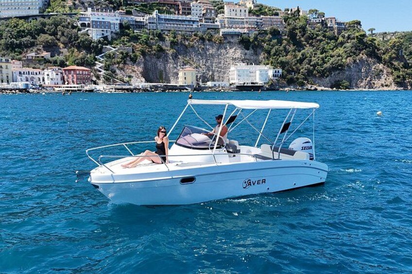 A white boat named 'Aver' on calm blue water with a coastal town in the background. 3