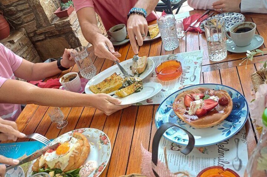 En gruppe mennesker spiser ved et træbord med tallerkener mad, glas vand og en menu. 1