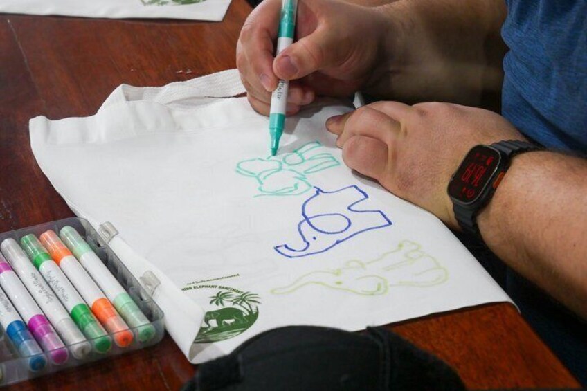 A person drawing on a white paper with markers, a watch on their wrist, and colored markers on the table. 2