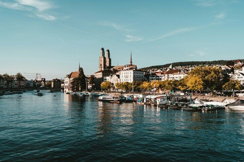 Un río con barcos, una iglesia con dos torres y edificios a lo largo de la orilla. 3