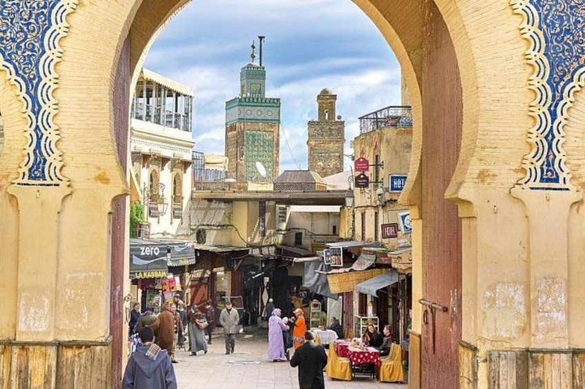 An archway with intricate blue and white patterns, leading to a bustling market street with people and shops. 2