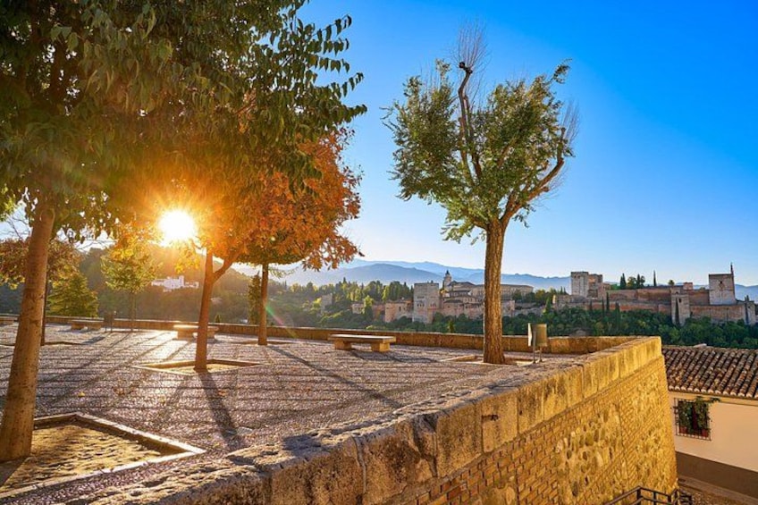 A courtyard with a tree, a stone wall, and a view of a distant town. 2