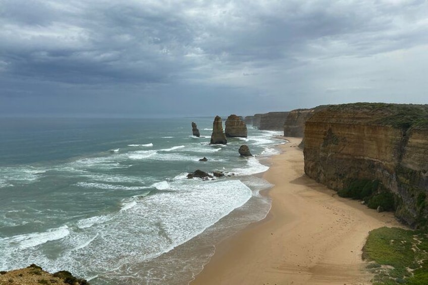 A coastal landscape with a sandy beach, ocean waves, and rock formations. 4