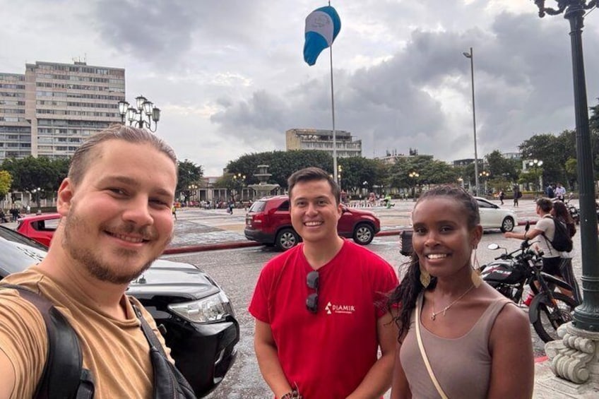 Tres personas de pie en un entorno urbano, con edificios y automóviles al fondo. 2