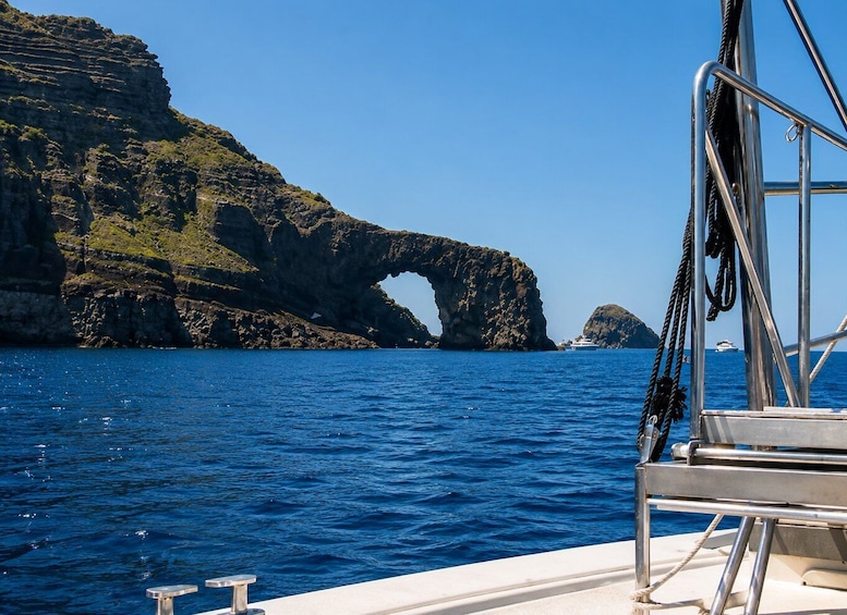 A boat with a view of a large rock formation with a natural arch over the water. 2