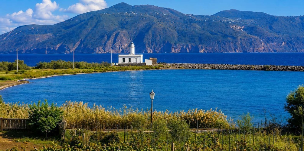 A coastal scene with a lighthouse, a clear blue sea, and a mountainous backdrop. 3