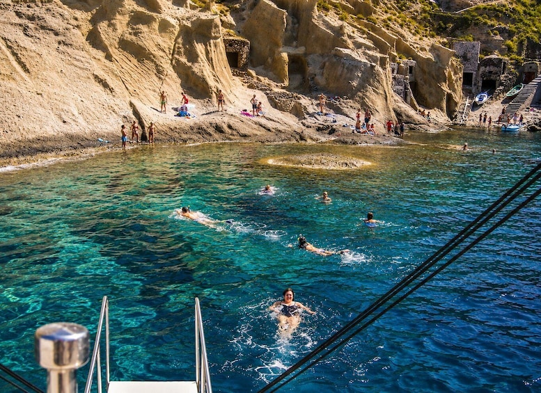 A clear blue pool surrounded by rocky cliffs with people swimming and sunbathing. 4