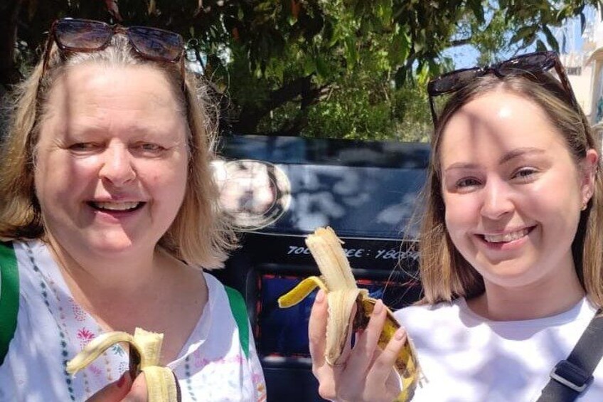 Two people holding bananas, with a vehicle in the background. 4