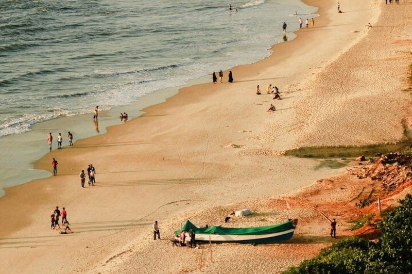 A beach with people walking and a green boat on the sand. 1
